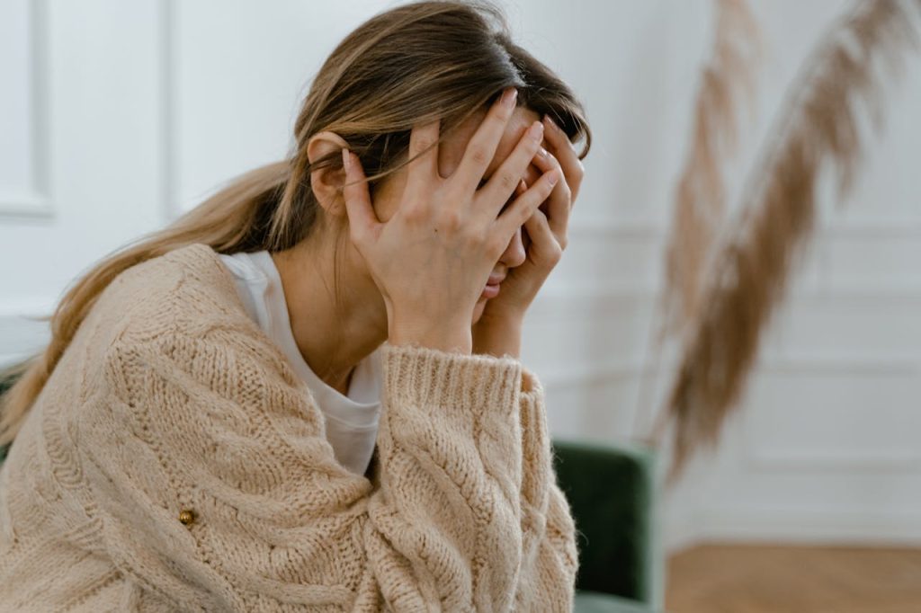 pexels photo 7699511 A woman sitting indoors covering her face in frustration, depicting stress and mental health challenges.